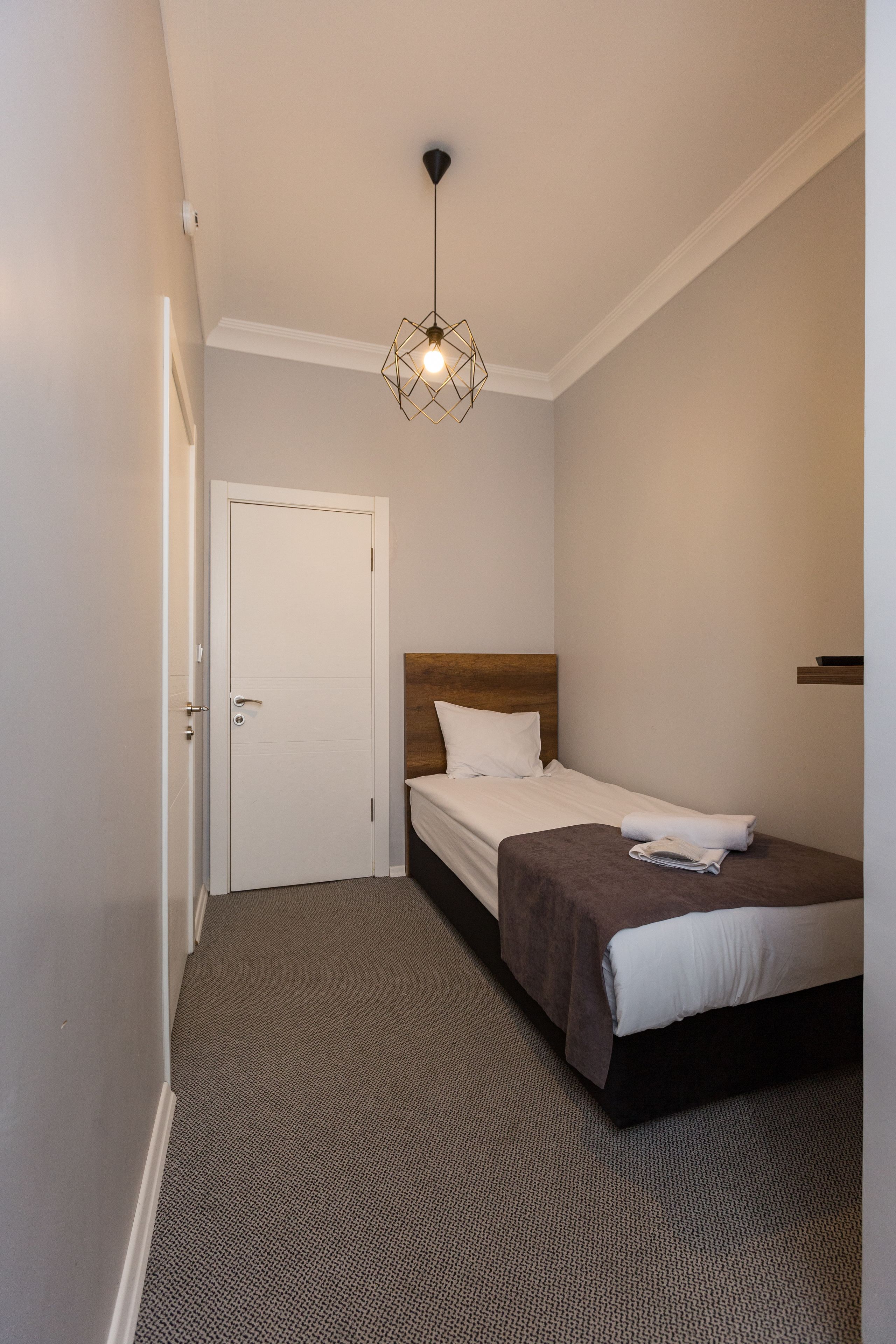 A hotel room with a bed, a door, a light fixture, and a carpeted floor.