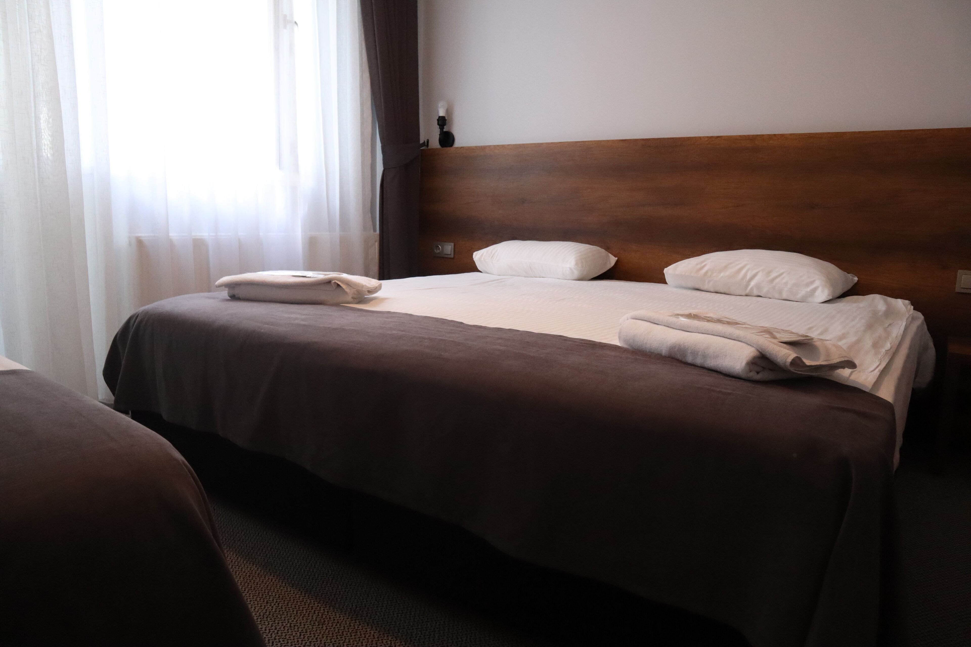 A hotel room with two beds, a wooden headboard, and a window with sheer curtains.
