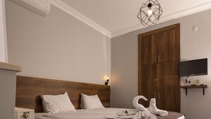 A neatly made bed with white linens, a wooden headboard, and a flat-screen TV on a shelf above it. - Baskent Konukevi (Ankara)