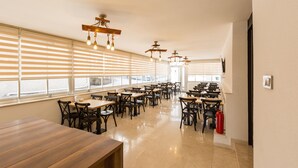 A spacious dining area with multiple tables and chairs, large windows with blinds, and hanging light fixtures. - Baskent Konukevi (Ankara)