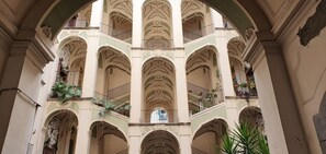 En atrium med flera våningsplan, utsmyckad med vackra arkitektoniska detaljer, inklusive valv och kolonner, samt balkonger med planterade blommor.
