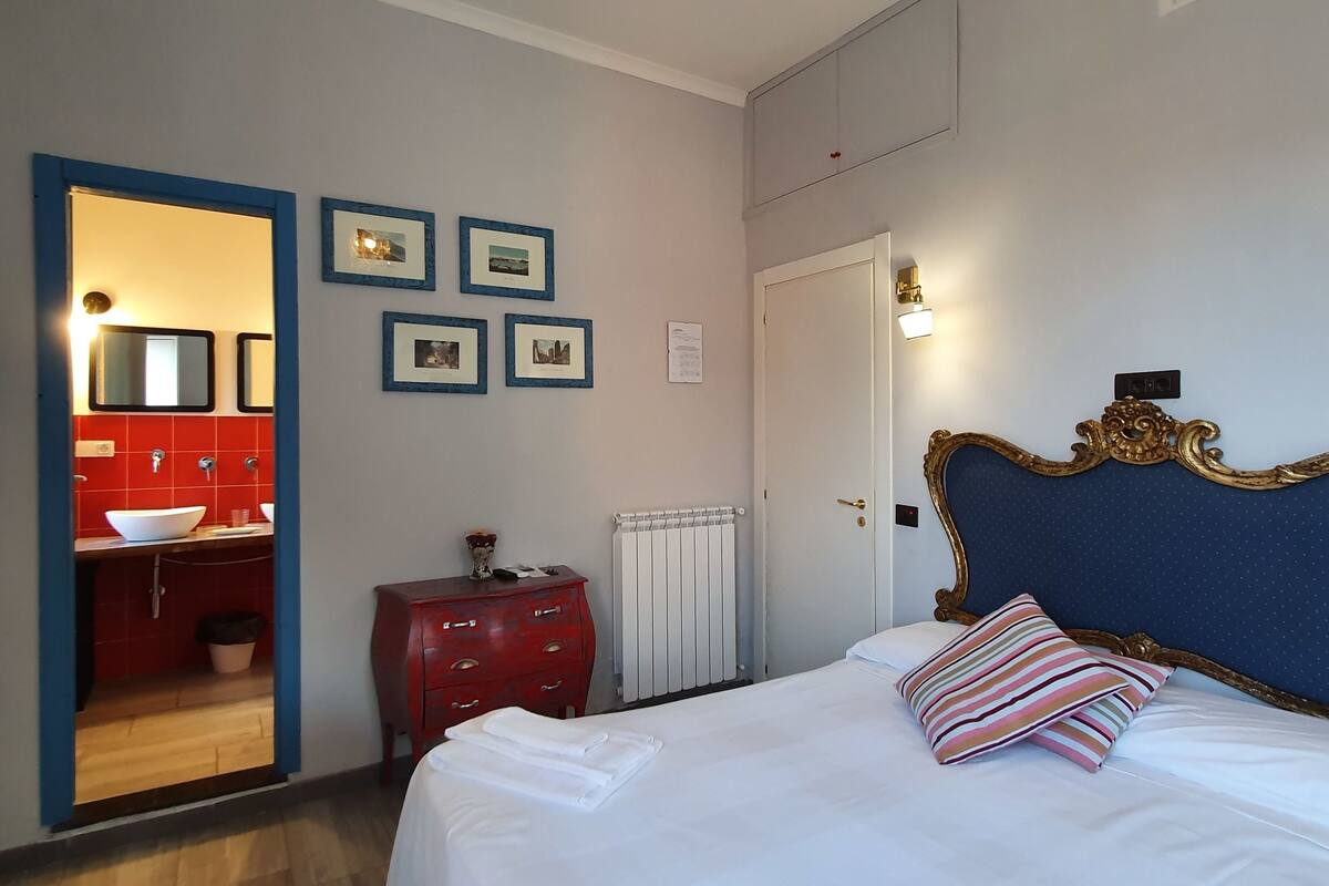 A bedroom with a large bed, a red dresser, a mirror, and framed pictures on the wall.