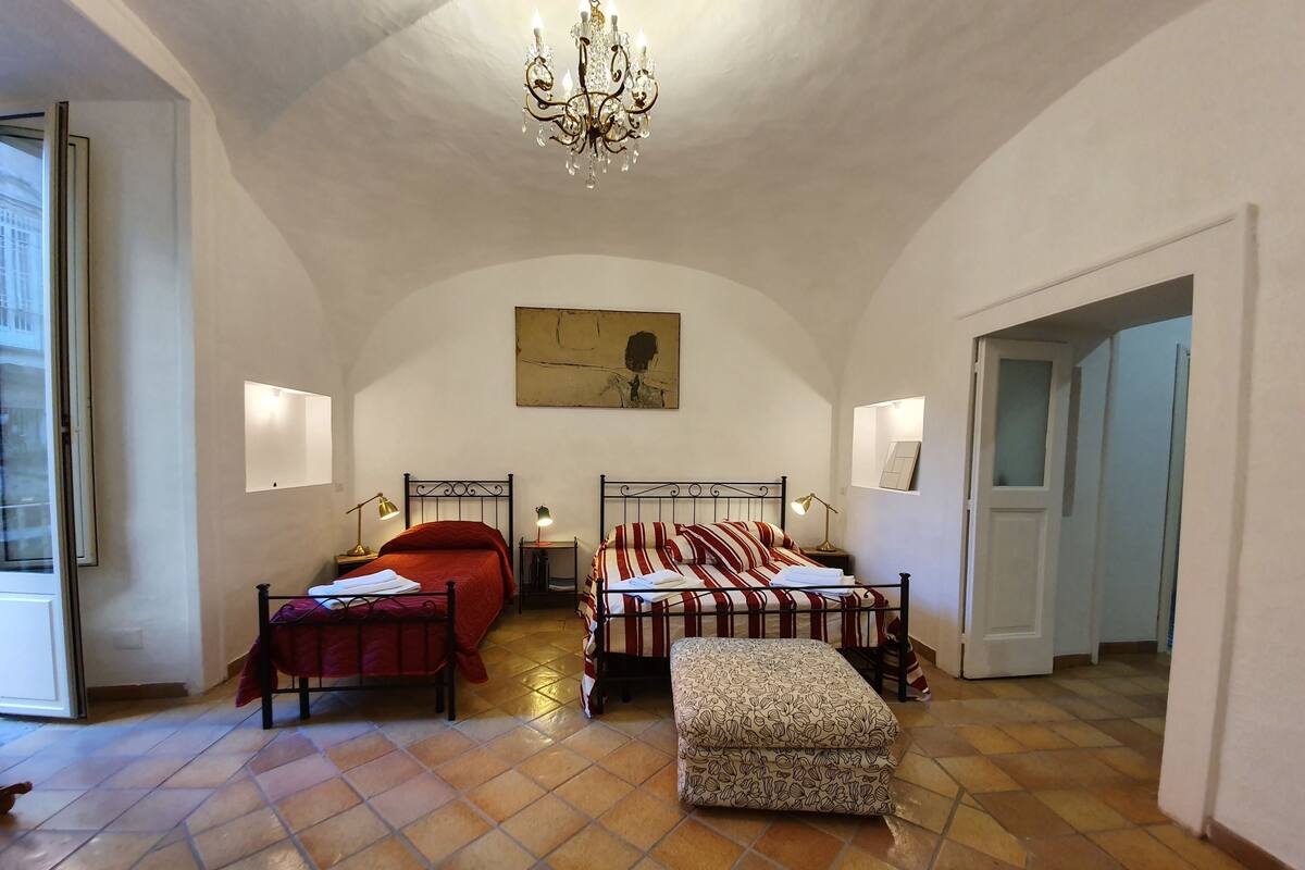 A bedroom with two beds, a chandelier, and a large painting on the wall.