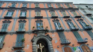 Un edificio de varios pisos con detalles arquitectónicos ornamentales, incluyendo balcones con barandillas y plantas en macetas.