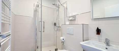 Ein modernes Badezimmer mit einer in Glas abgeschirmten Dusche, einer weißen Toilette und einem Waschbecken mit Spiegel darüber.