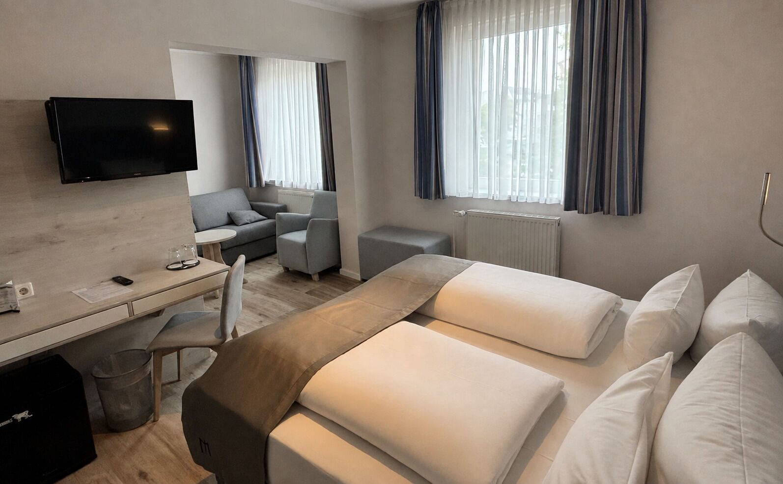 A hotel room with a bed, a desk, a chair, a television, and a window with curtains.