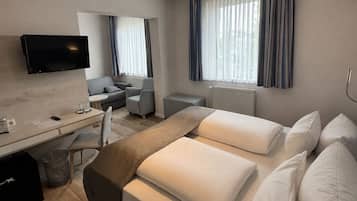 Habitación de hotel con cama, escritorio, silla, televisor y ventana con cortinas.