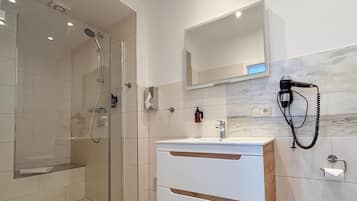 Un bagno moderno con doccia vetrata, un mobile lavabo bianco con piano in marmo e un asciugacapelli a parete.