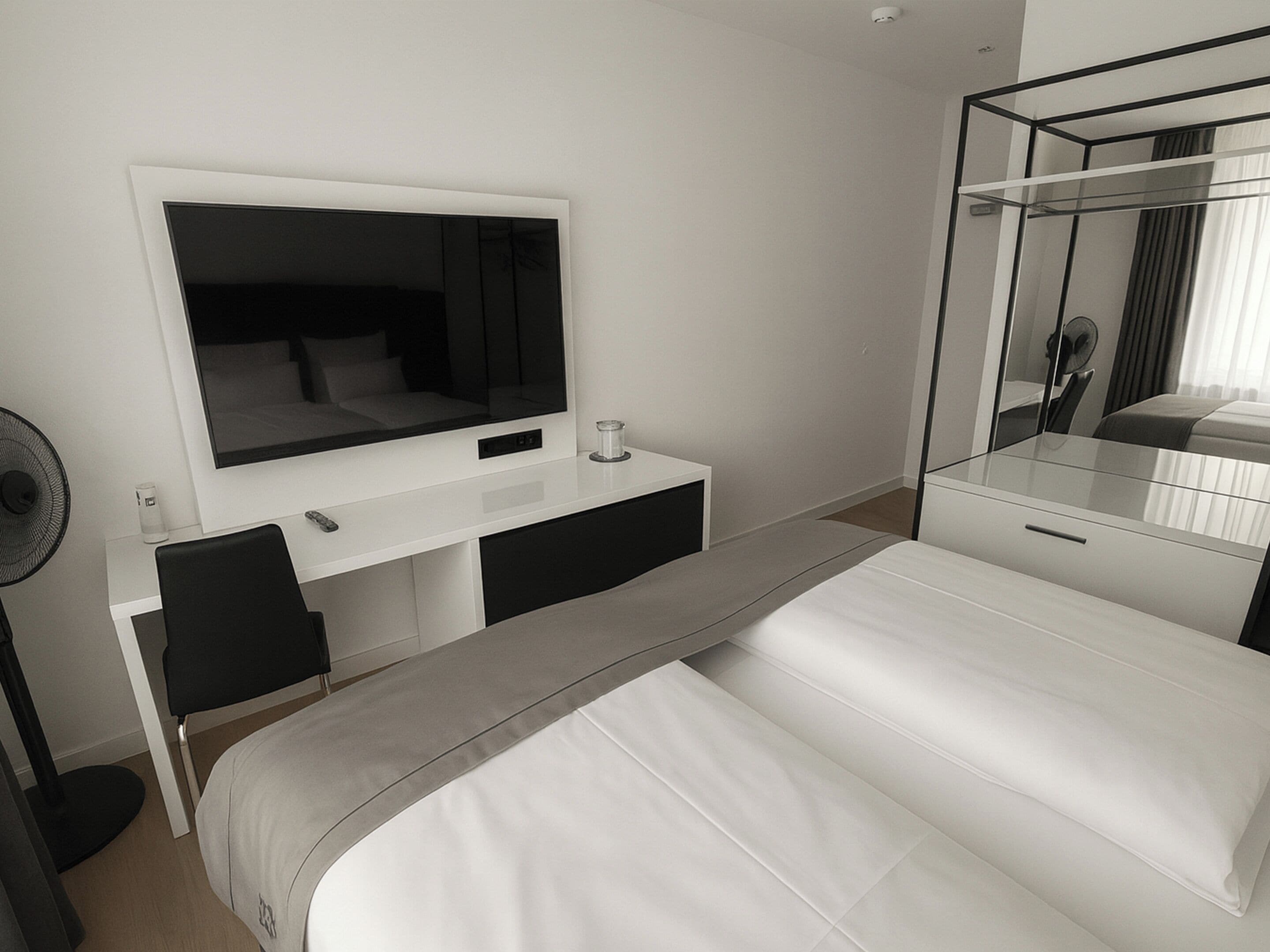 Ein modernes Hotelzimmer mit einem großen Bett, einem Schreibtisch, einem Flachbildfernseher, einem Spiegel und einem Ventilator.
