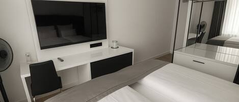 A modern hotel room with a large bed, a desk with a flat-screen TV, a mirror, and a fan.