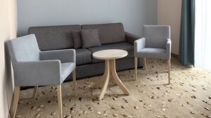 Una habitación moderna con un sofá gris y dos sillones, una pequeña mesa redonda y una pared con el texto 