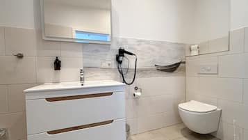 A modern bathroom with a white vanity, a mirror, a toilet, and a wall-mounted hairdryer.