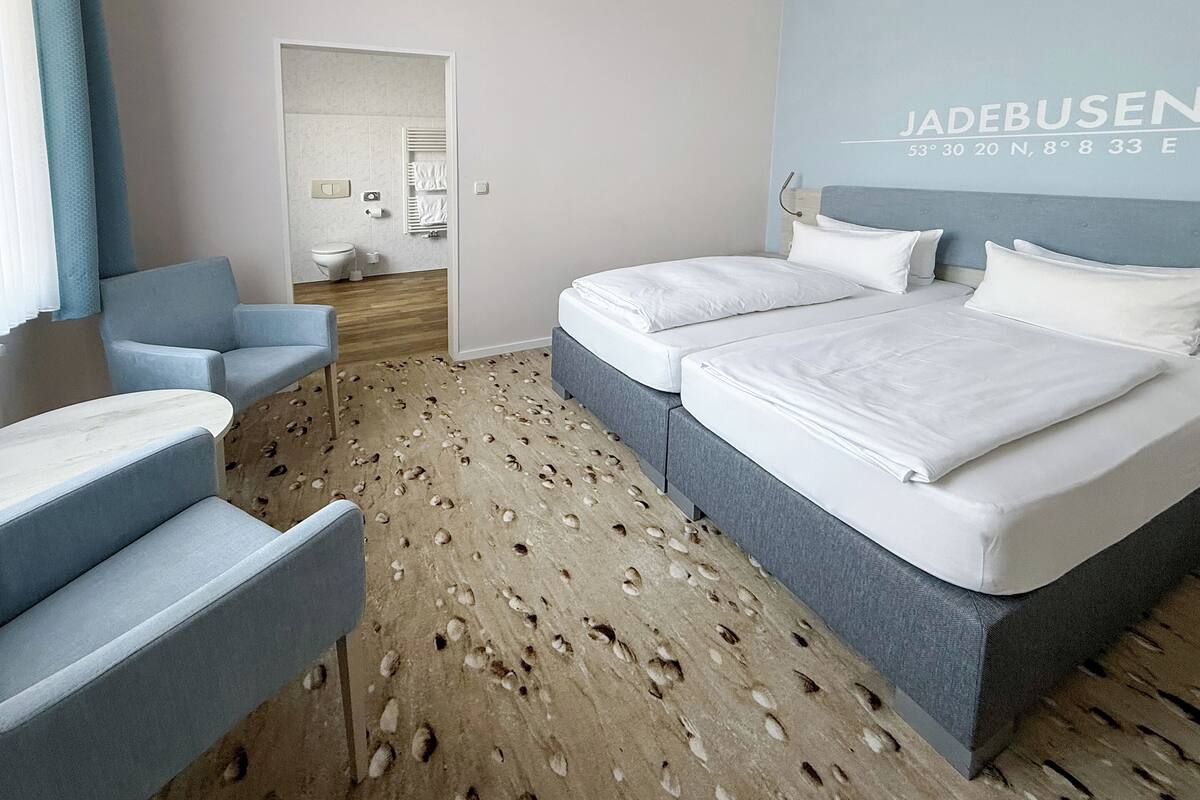Ein modernes Hotelzimmer mit einem großen Bett, zwei Nachttischen, einem Sessel und einem durch eine offene Tür einsehbaren Badezimmer.