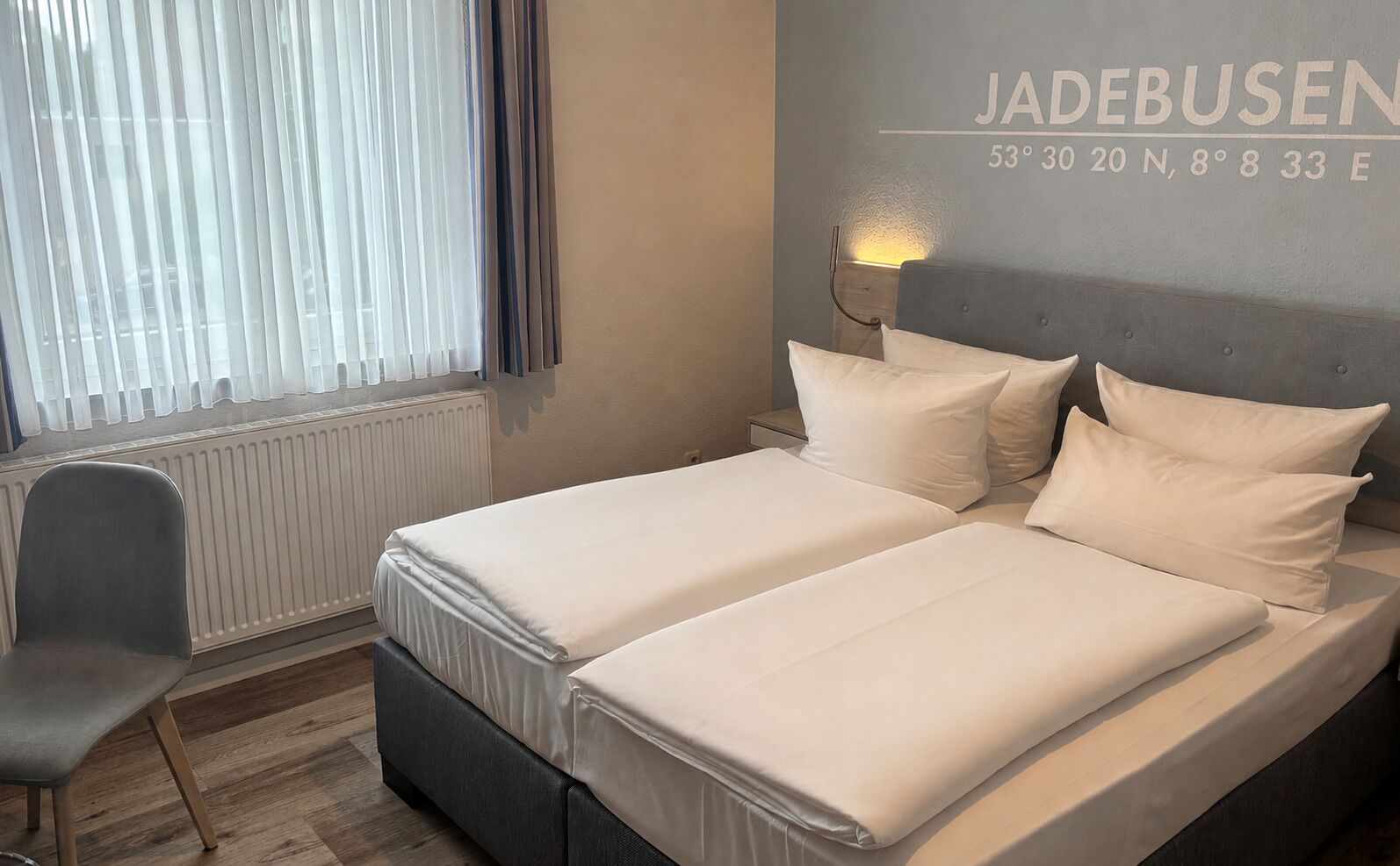 A double bed with white bedding, a bedside lamp, and a chair in a hotel room.