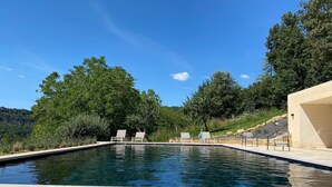 Une piscine entourée d’arbres et bordée d’une colline, avec des chaises longues à proximité.