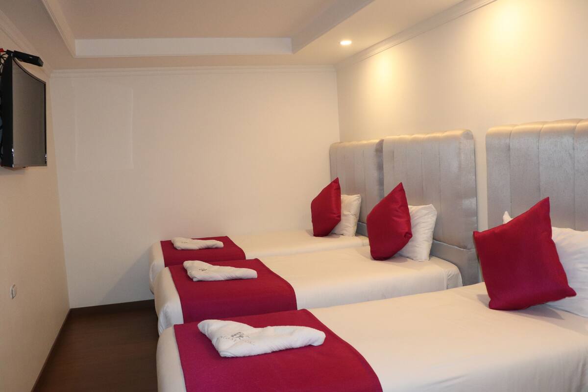 A hotel room with four beds aligned in a row, each with white bedding and red pillows.