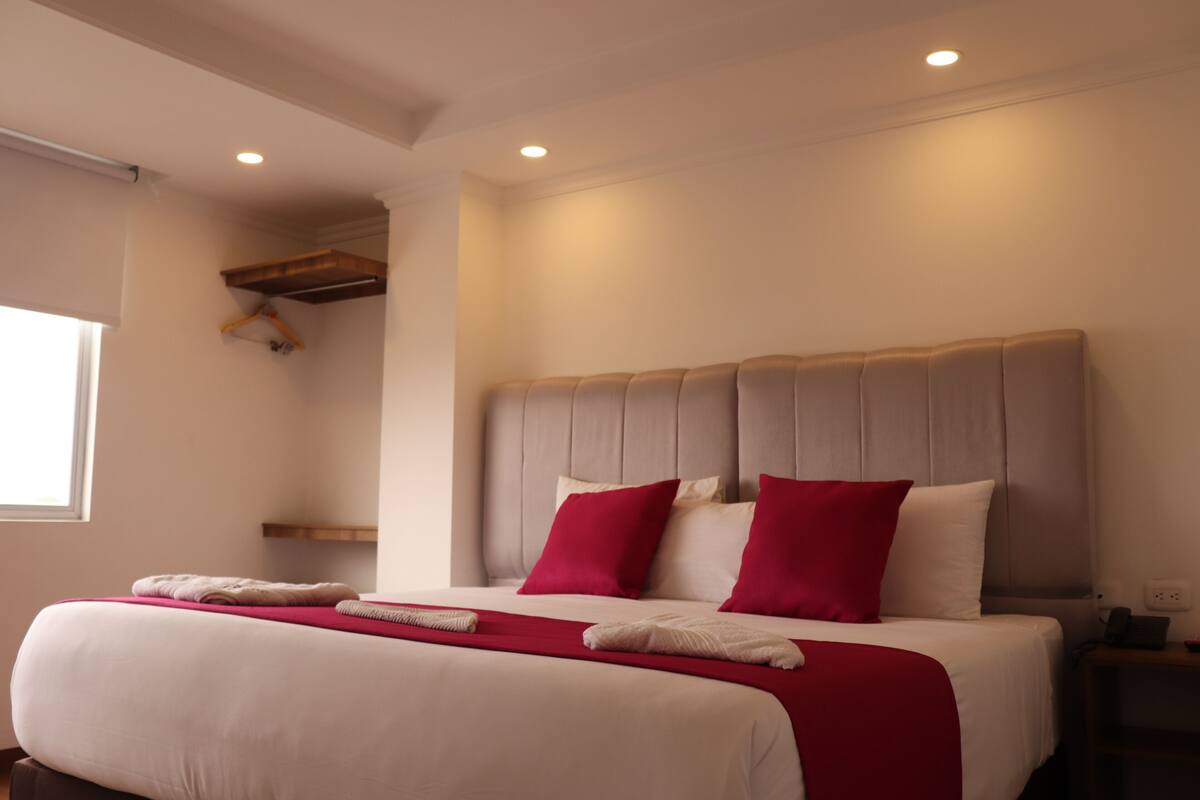 A neatly made bed with a red and white bedspread, a wooden headboard, and a bedside table with a lamp.