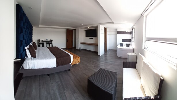 Ein modernes Hotelzimmer mit einem großen Bett, einer Couch, einem Schreibtisch und einem an der Wand montierten Fernseher.