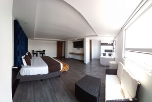 Ein modernes Hotelzimmer mit einem großen Bett, einer Couch, einem Schreibtisch und einem an der Wand montierten Fernseher.