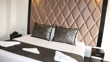 Habitación de hotel con una cama grande, cabecera con diseño de rombos, dos almohadas decorativas y una mesita de noche con un teléfono.