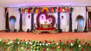 A stage with a red sofa, floral decorations, and draped curtains. - Sai Arya Lodging & Hall (Mangaluru)