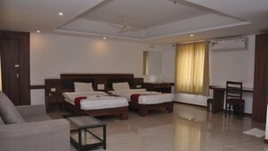 A hotel room with two single beds, a sofa, a small table, a desk, and a ceiling fan. - Sai Arya Lodging & Hall (Mangaluru)