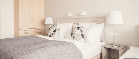 A modern hotel room with a large bed, bedside tables, a wardrobe, and a ceiling light.