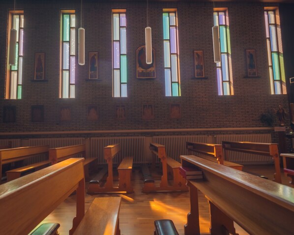 Interior de una iglesia con bancas de madera, vidrieras y lámparas colgantes.