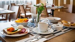 Un esmorzar amb una torrada, fruita, un croissant, una tassa de cafè i un vas amb flors damunt d'una taula.