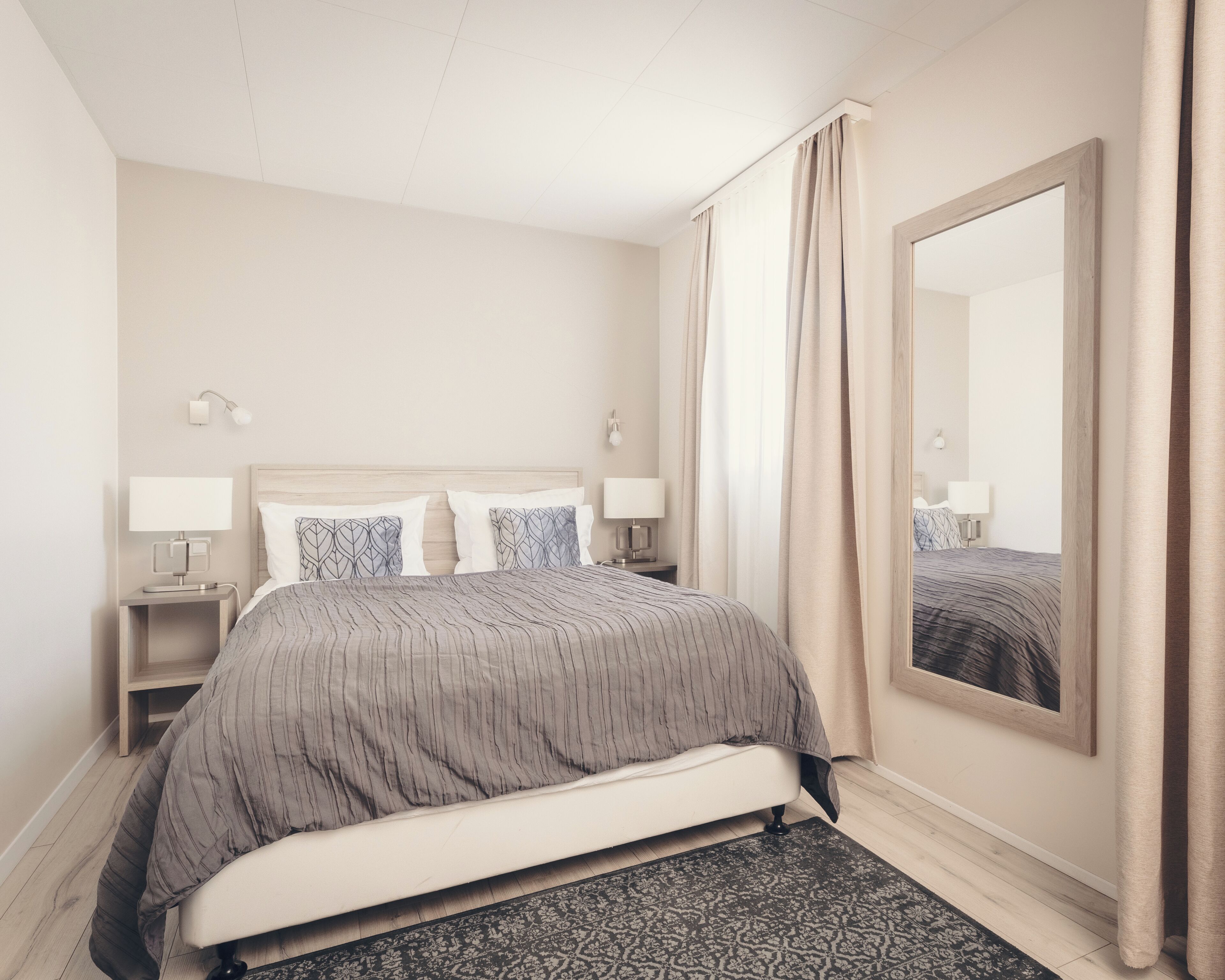 Een hotelkamer met een bed, nachtkastjes, een grote spiegel en een kamerkleed met dessin.