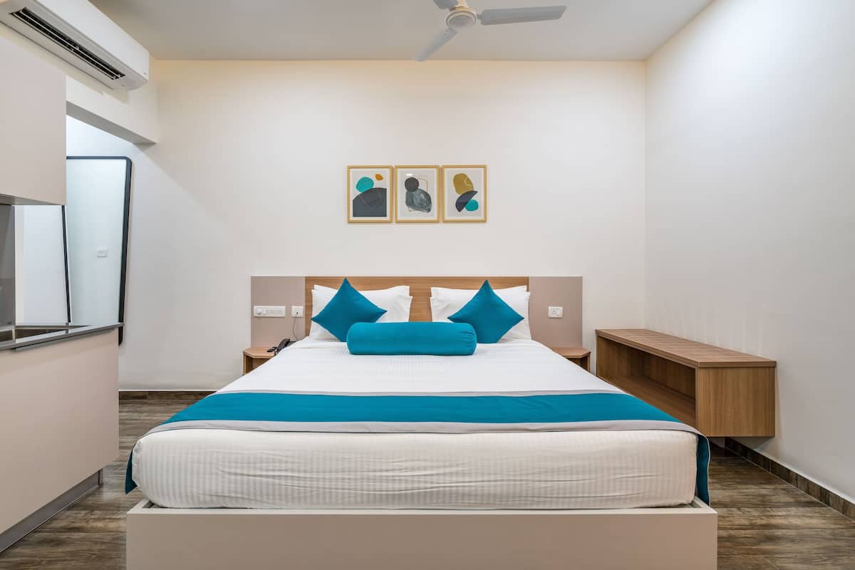 Quarto de hotel bem arrumado com cama, mesas de cabeceira, ar condicionado fixado na parede e ventilador de teto.