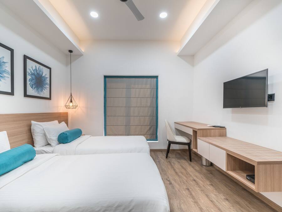 Une chambre d’hôtel moderne équipée de deux lits, d’un bureau, d’une chaise, d’une télévision et d’une fenêtre avec des stores.