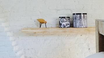 A white brick wall with a wooden shelf holding a small wooden stool and two cylindrical containers.