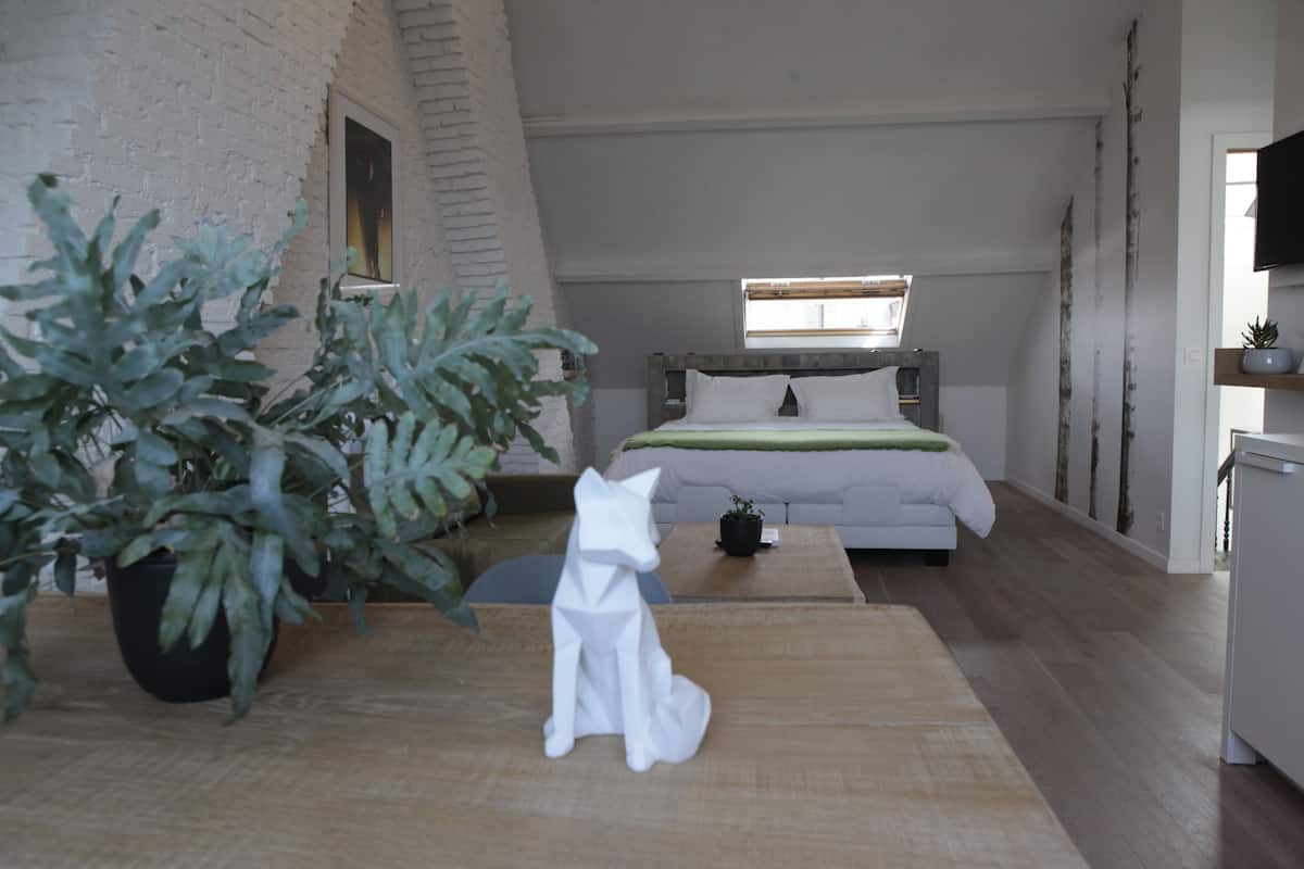 Een moderne loft slaapkamer met een schuine plafond, een bed met een groene deken, een witte bank, een houten tafel en een potplant.
