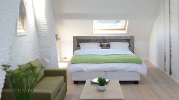 Una camera da letto con un lucernario, un letto con coperta verde, un tavolino con una pianta e un divano verde.