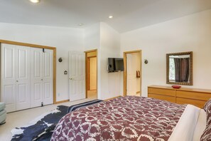 Un dormitorio con una cama grande, un aparador de madera, un televisor fijado en la pared y una puerta que da a otra habitación.