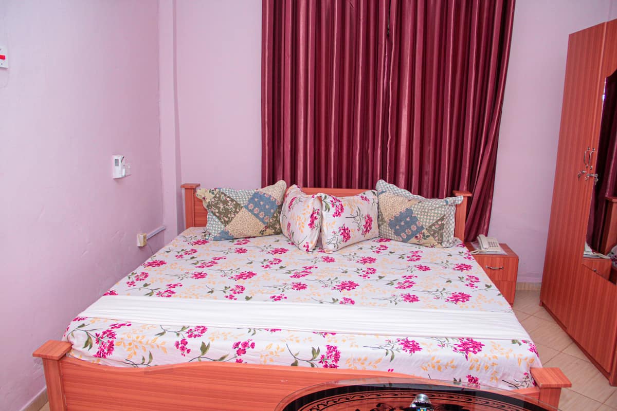 A bedroom with a wooden bed, floral bedding, a red curtain, a wooden wardrobe, and a bedside table with a phone.