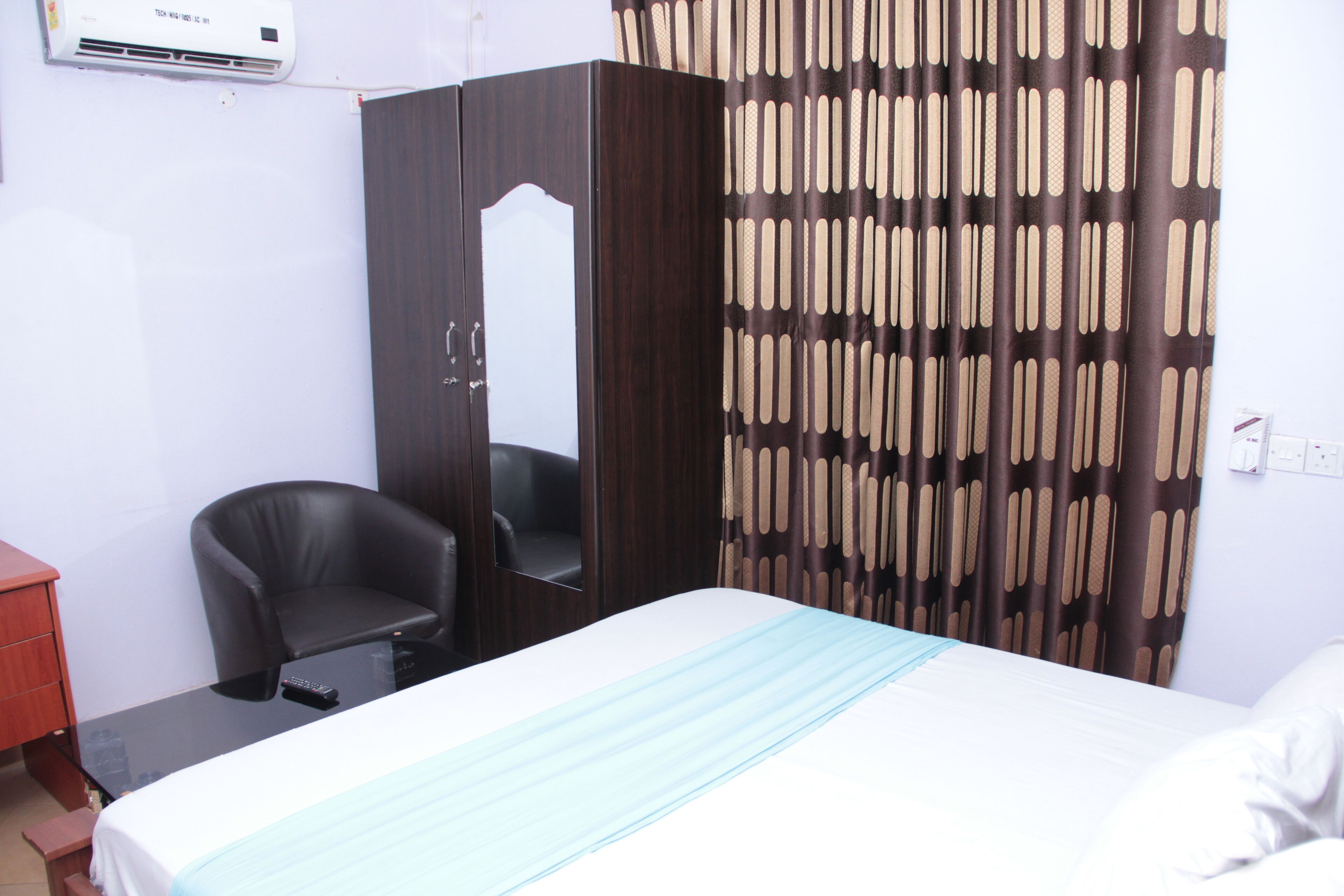 A hotel room with a bed, a desk, a chair, a wardrobe, and a curtain.
