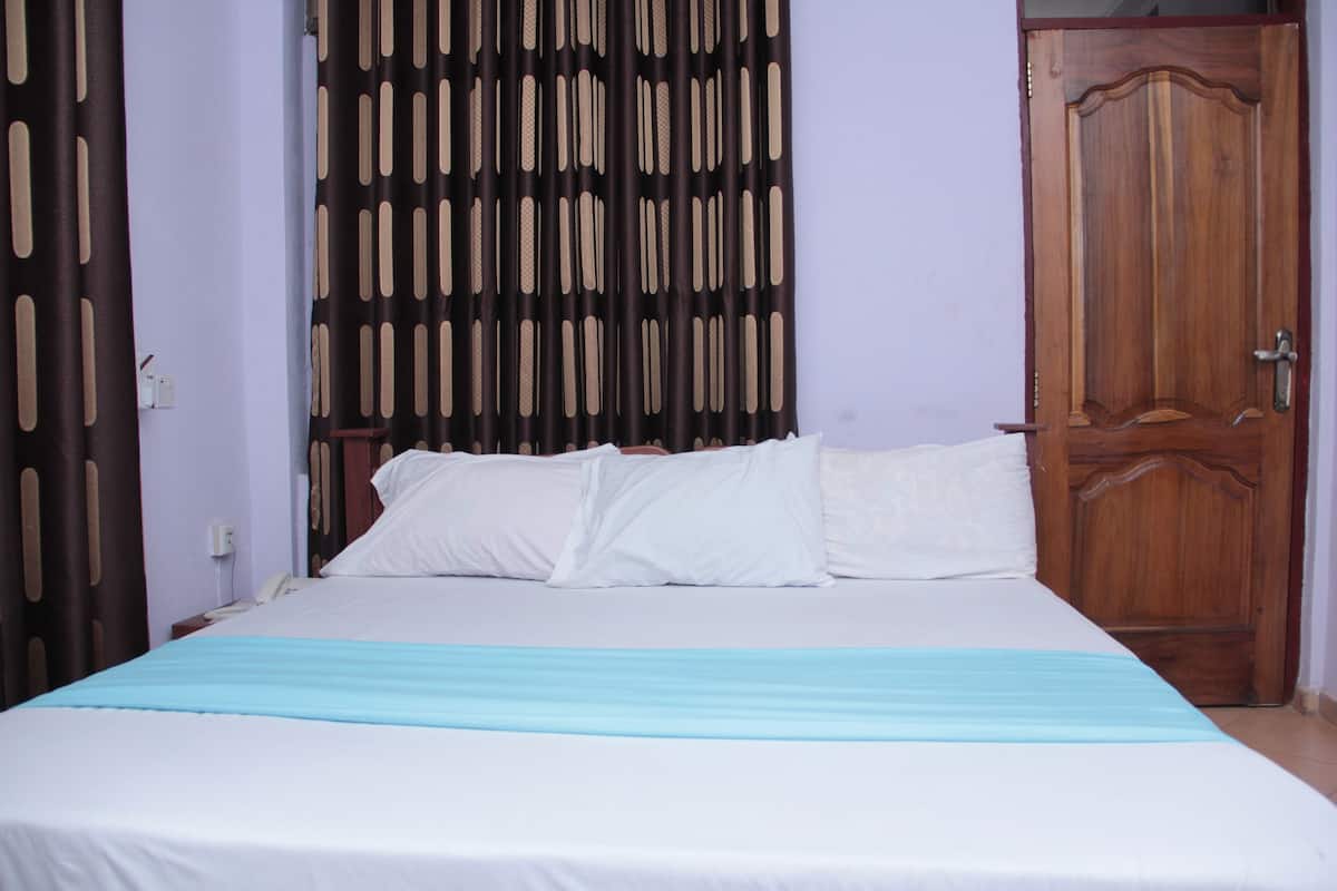 A bed with white bedding and a blue runner, a wooden door, and a patterned curtain.