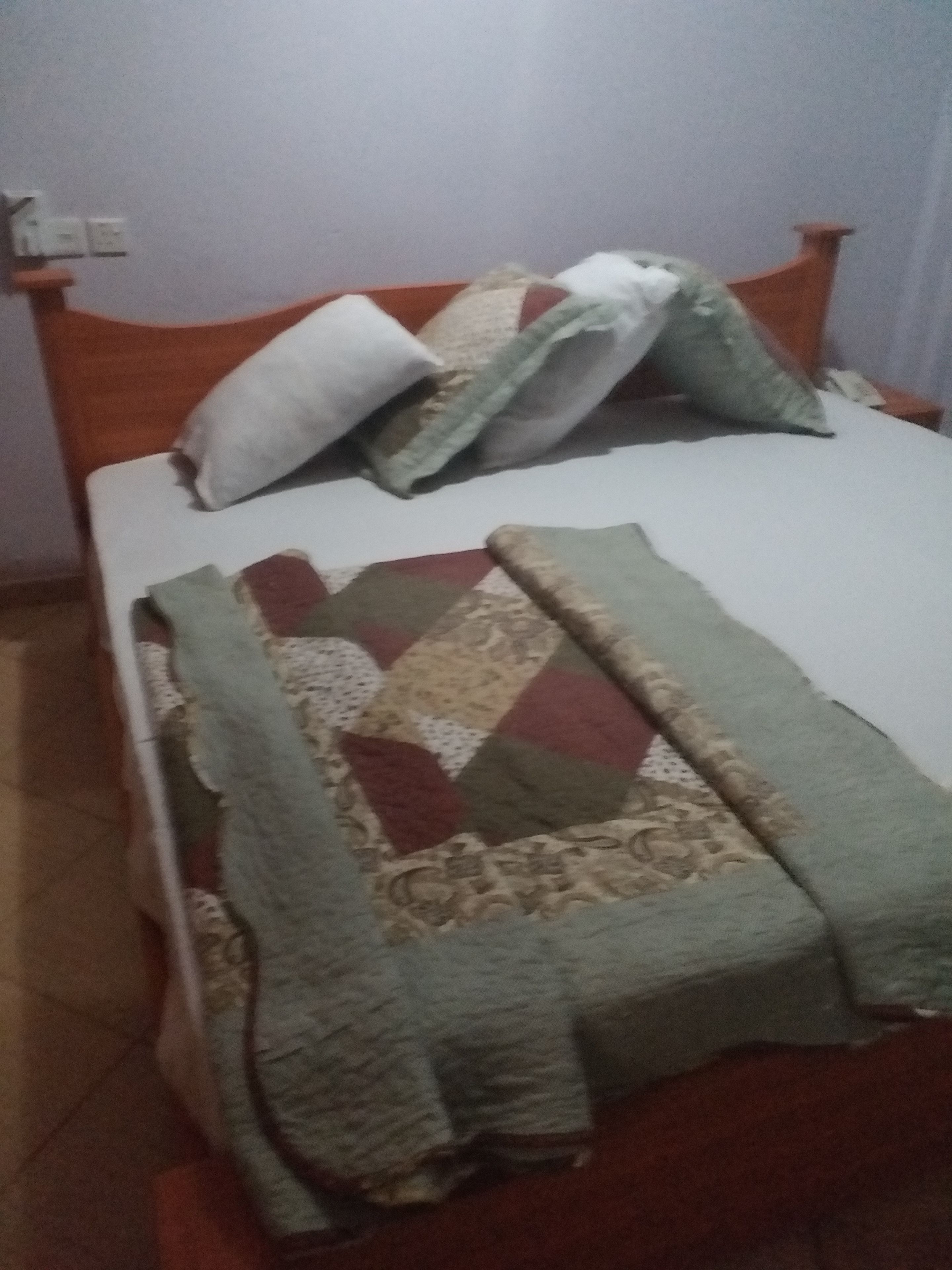 A bed with a quilt and pillows, a wooden headboard, and a wall socket.