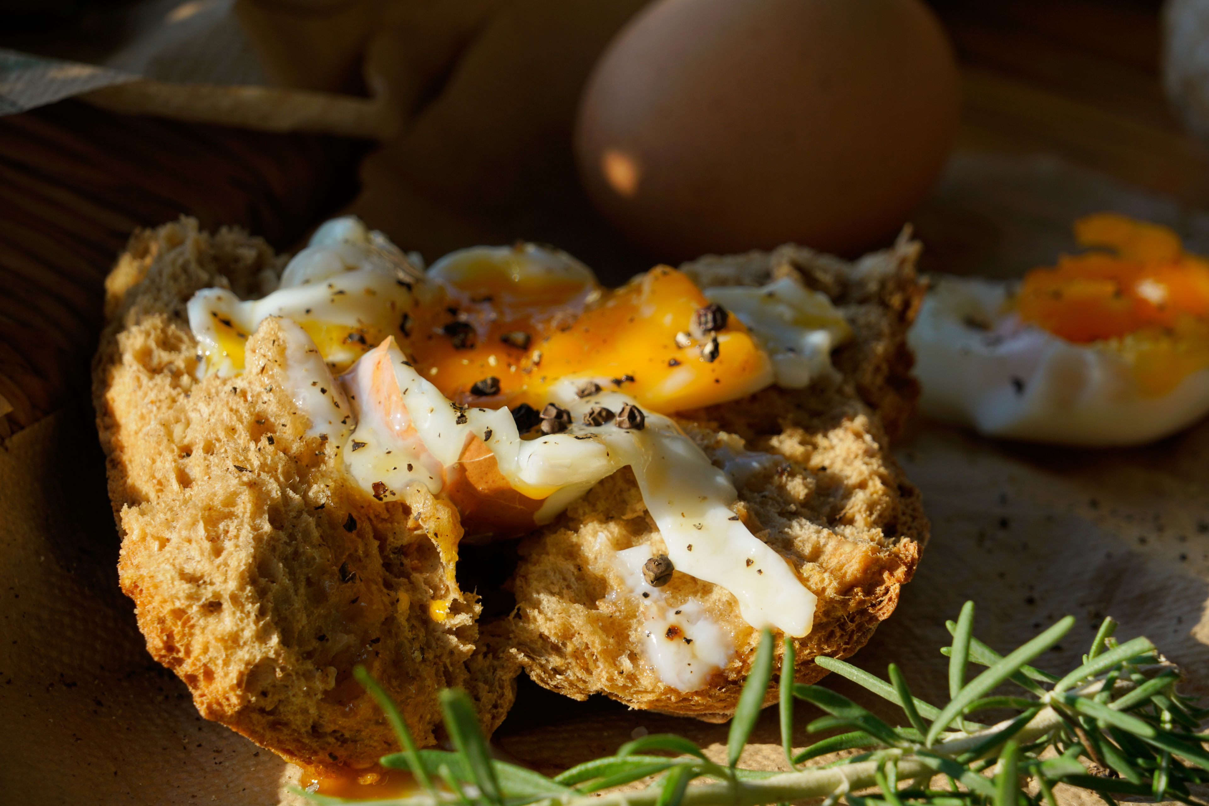 A breakfast dish with eggs and cheese on a slice of bread, accompanied by a whole egg and some herbs.
