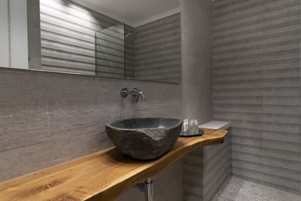 Een moderne badkamer met een stenen wasbak op een houten aanrecht, een spiegel en een douchehoek.