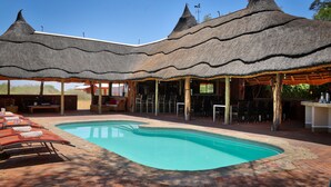 A pool area with lounge chairs and a thatched-roof pavilion. - Guest Farm Kiripotib (Windhoek)