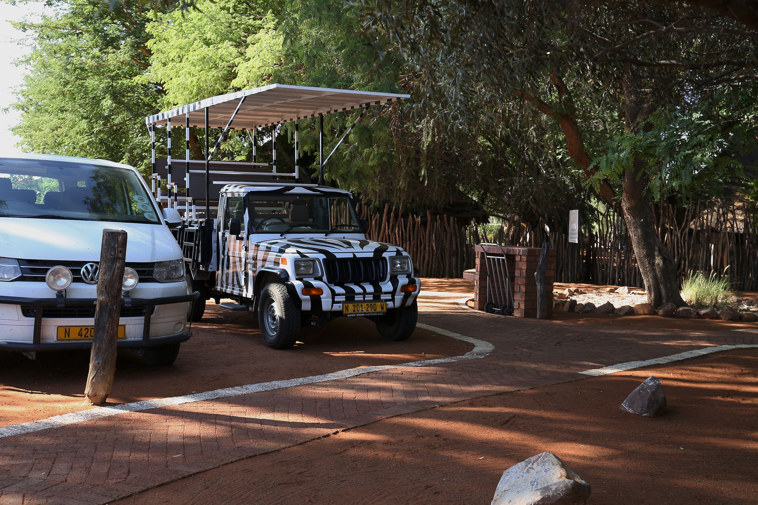 A safari vehicle parked at a campsite with a covered area and trees in the background.