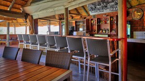An outdoor bar area with wicker chairs and a wooden table, a brick wall with a zebra mural, and a wooden ceiling. - Guest Farm Kiripotib (Windhoek)