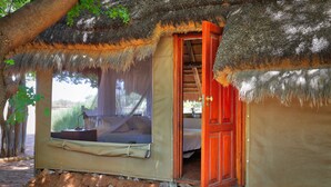 A thatched-roof structure with a bed and a window overlooking a natural landscape. - Guest Farm Kiripotib (Windhoek)