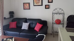 A living room with a black sofa, red and grey cushions, a small table with a lamp, and a metal stand with a red bowl. - T2 curists classified 3 * Res secure 10 minutes walk from the thermal baths (Lamalou-les-Bains)