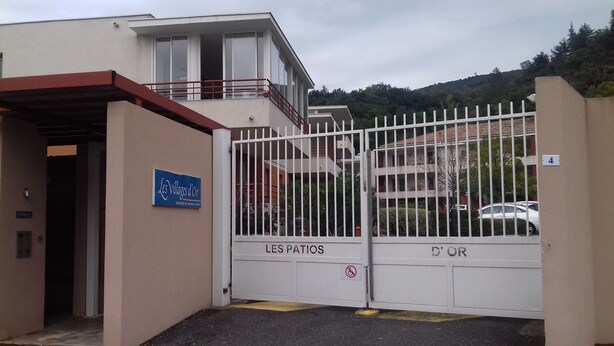 A gated entrance to a building with a sign reading "Les Villages d'Or" and "Specialiste du logement lentement." - T2 curists classified 3 * Res secure 10 minutes walk from the thermal baths (Lamalou-les-Bains)