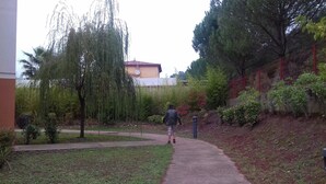 A pathway in a landscaped area with trees and a building in the background. - T2 curists classified 3 * Res secure 10 minutes walk from the thermal baths (Lamalou-les-Bains)