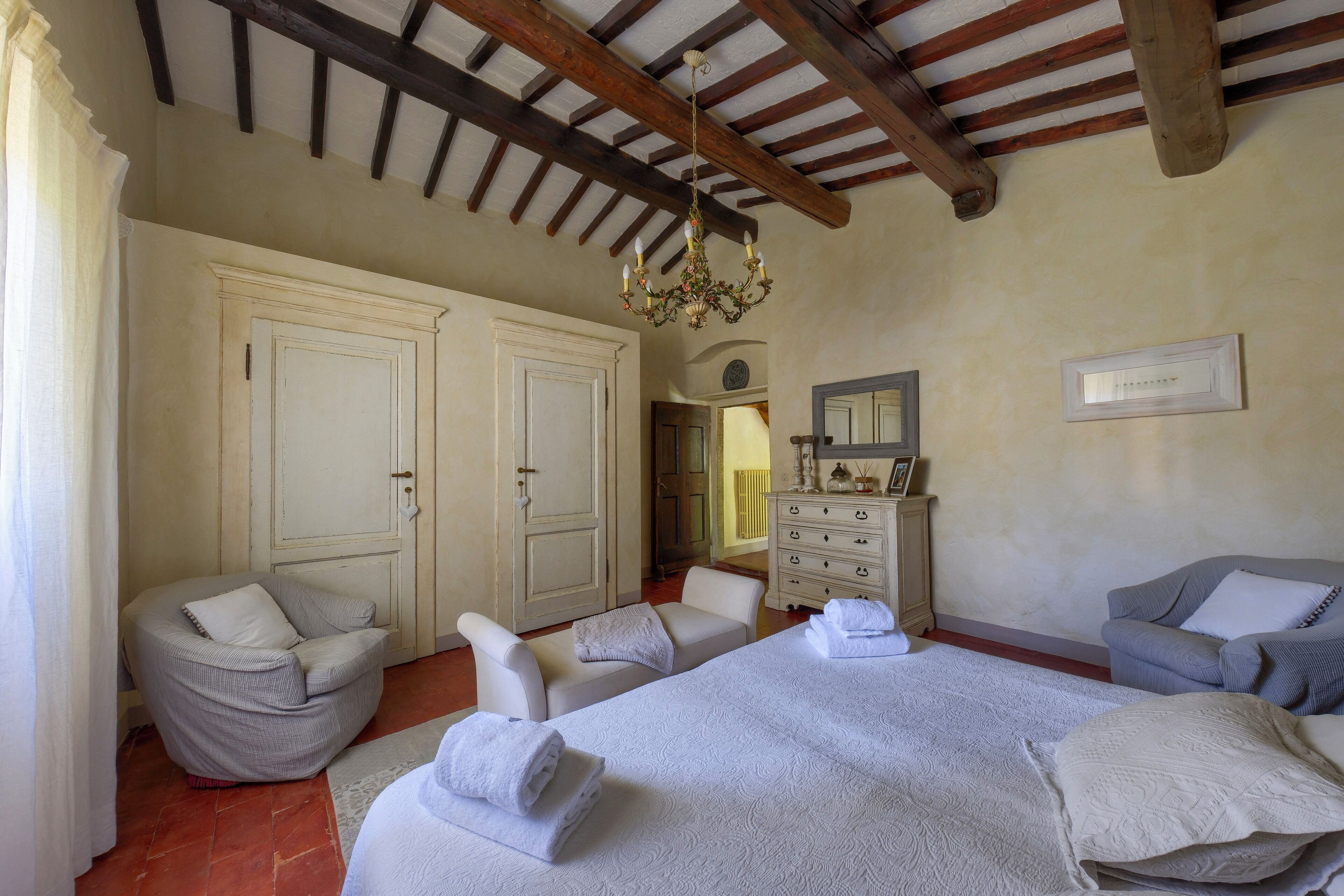 Una camera da letto con un letto grande, due poltrone, una cassettiera e un lampadario.
